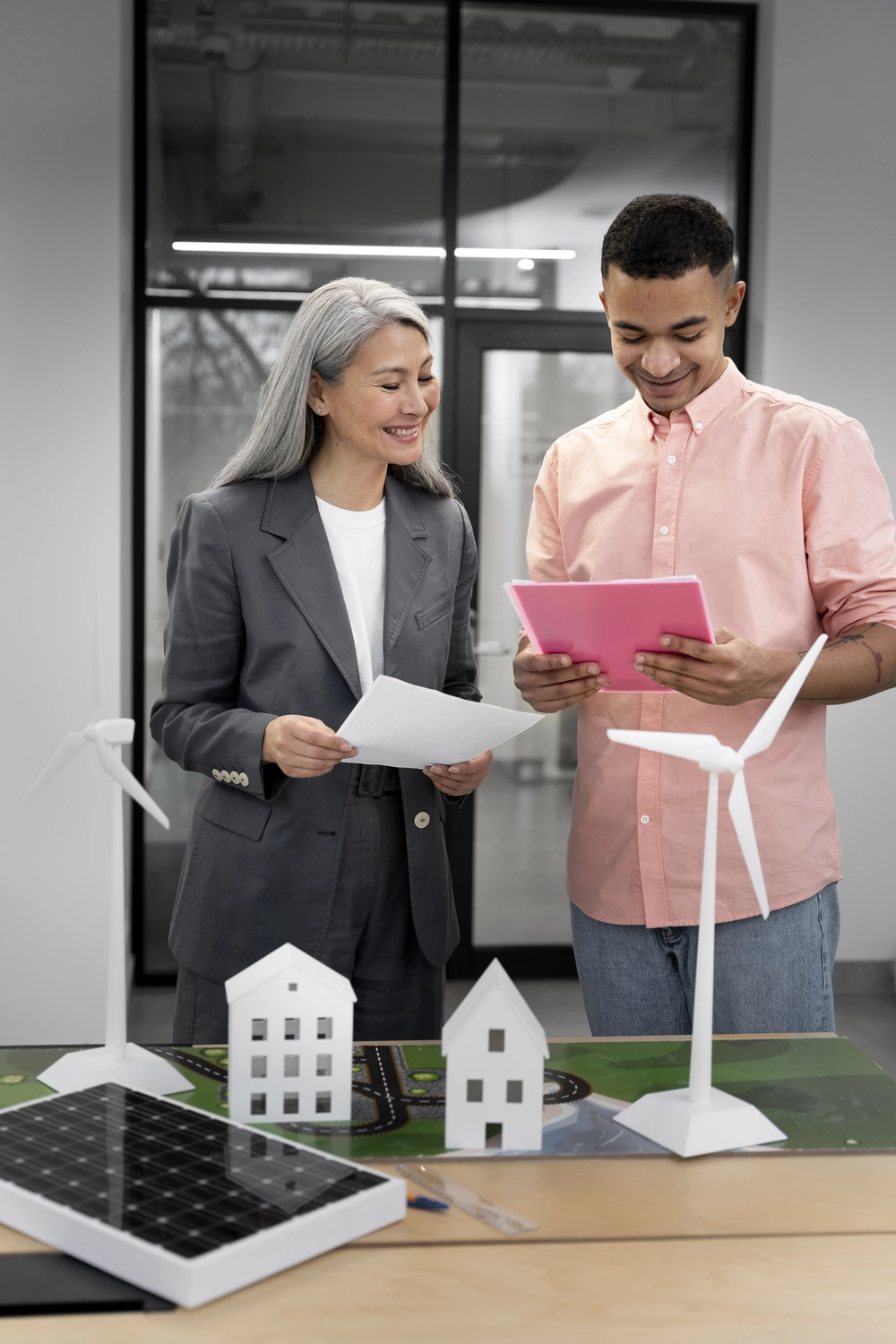 Slooyer GmbH – Gebäudeenergieberater – Dieses Bild zeigt zwei Fachleute, einen Energieberater und einen Ingenieur, die an einem maßstabsgetreuen Modell, das Windturbinen und ein Solarpanel umfasst, ein Projekt für erneuerbare Energien diskutieren