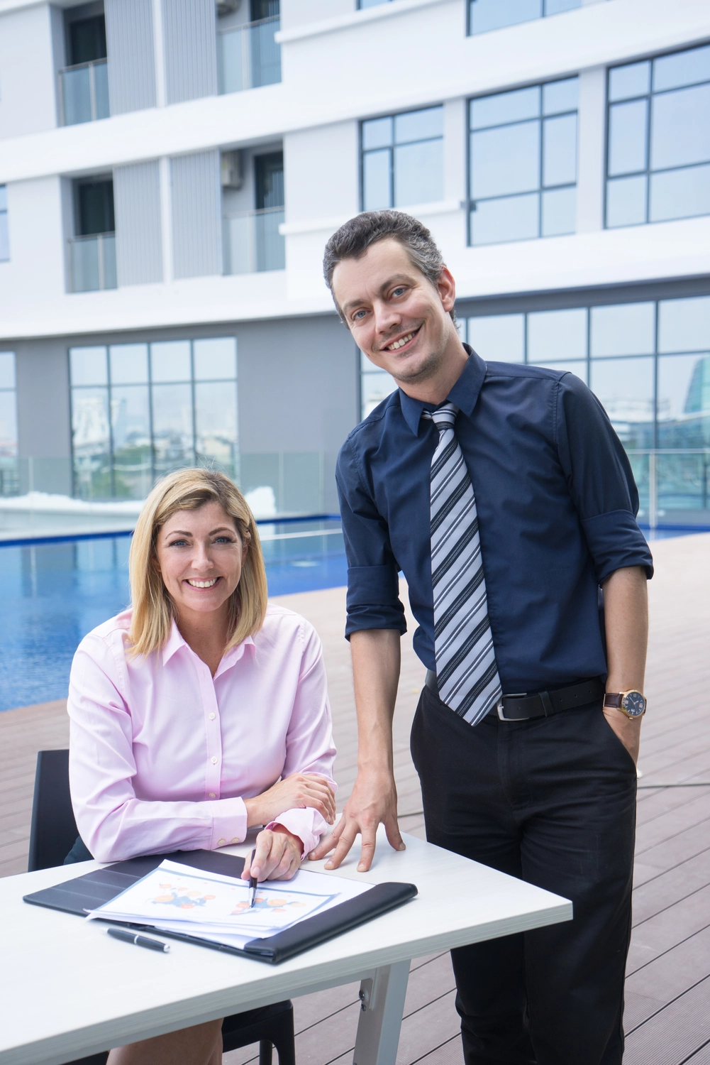 Slooyer GmbH - Gebäudeenergieberater - Dieses Bild zeigt zwei Kollegen, die für ein Foto lächeln, während sie im Freien gemeinsam an einem Bericht arbeiten.